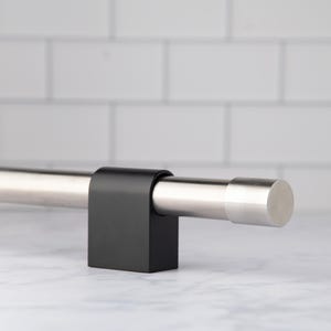May include: A silver-colored metal rod with a rounded end, held in place by a black square bracket. The rod is approximately 30 inches long. The background features a white tile wall and a marble surface.