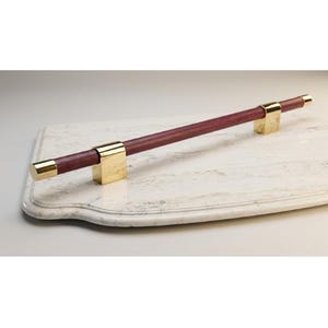 May include: A serving tray with a rectangular marble surface and a dark red wooden handle. The handle is accented with gold-colored metal brackets and end caps. The tray is designed for serving food or displaying items.