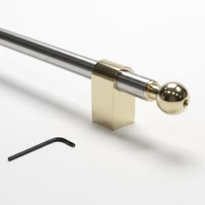 May include: A cabinet pull featuring a long, cylindrical silver-toned bar held by two gold-toned rectangular mounts. The ends of the bar are capped with gold-toned spherical finials. A small black L-shaped hex key is positioned below the pull.