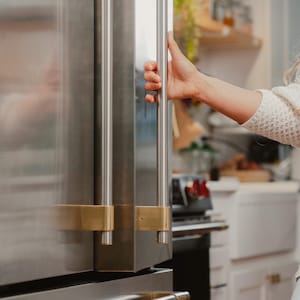 May include: A stainless steel refrigerator door featuring long, vertical cylindrical handles with brushed brass mounting brackets. The refrigerator has a sleek metallic finish and a horizontal handle on the lower freezer drawer section.