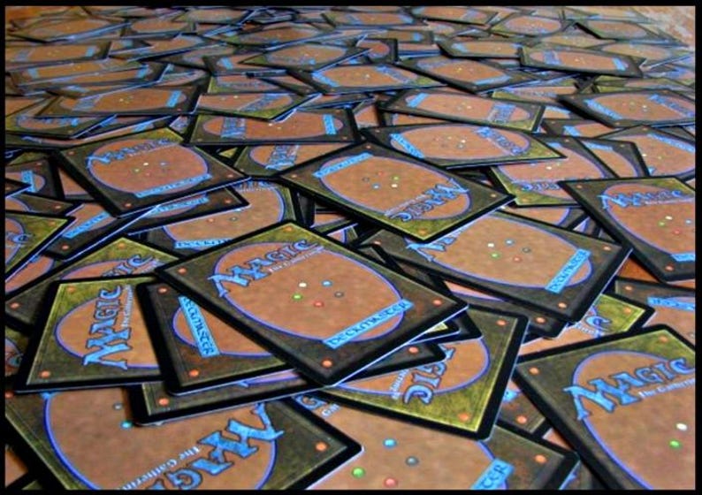 May include: A large pile of Magic: The Gathering trading cards. The cards have a brown and blue design on the back with the word "MAGIC" in a stylized font. The fronts of the cards are not visible.