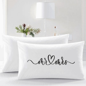 May include: Two white pillowcases with black embroidery. The top pillowcase has the text "mr & mrs" with a heart in between the words.