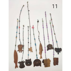 Op de afbeelding: Een verzameling houten hangornamenten met verschillende dierfiguren, waaronder vissen, olifanten en beren. Elk ornament hangt aan een ketting versierd met kleurrijke kralen. Het nummer "11" is rechtsboven zichtbaar.