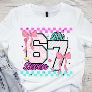 May include: White t-shirt featuring the numbers "67" with a floral pattern and the words "Six" and "Seven". The design includes pink bows, stars, and a checkered border in pink and turquoise.