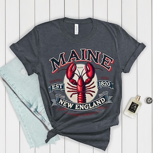 May include: A dark heather grey t-shirt featuring a vintage-style graphic of a lobster and the text "Maine Coastal Est 1820 Vibes New England".