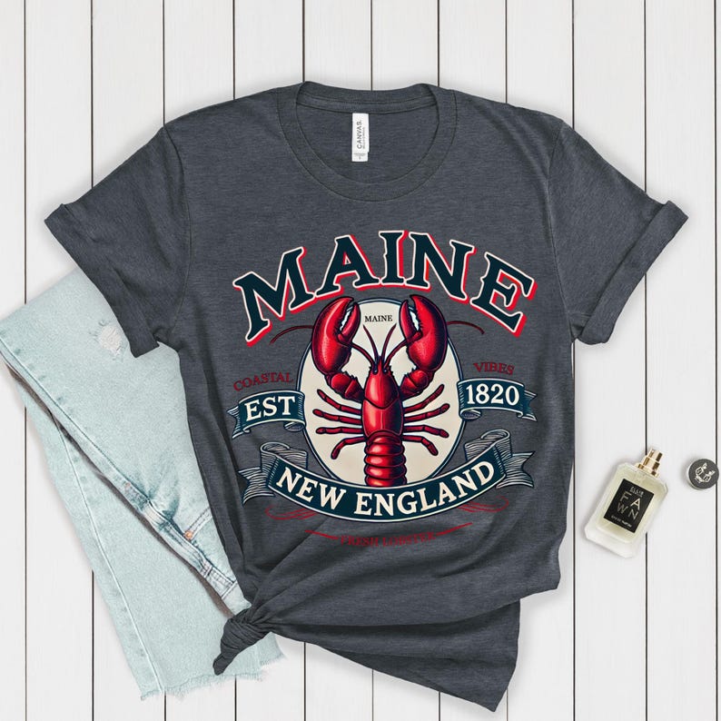 May include: A dark heather grey t-shirt featuring a vintage-style graphic of a lobster and the text "Maine Coastal Est 1820 Vibes New England".