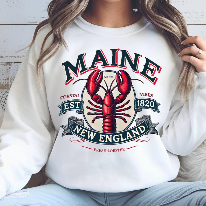 May include: White sweatshirt with a graphic design featuring a red lobster, the words "Maine", "Coastal Est 1820", "New England", and "Fresh Lobster", and the text "Maine" in a circle.