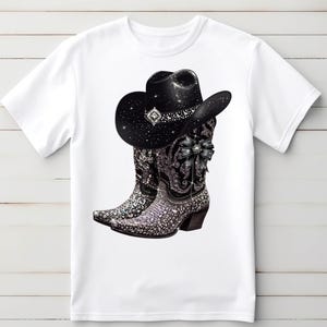 May include: White t-shirt with a black cowboy hat and boots with rhinestones. The hat and boots are decorated with a black bow.