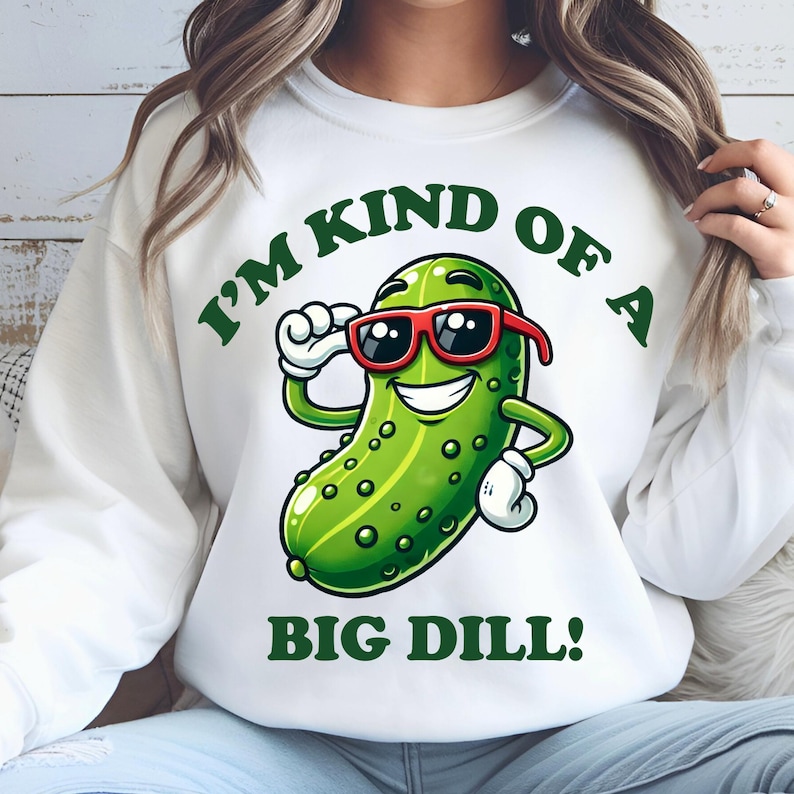 Może przedstawiać: Biała bluza z zielonym kresk&oacute;wkowym og&oacute;rkiem w okularach przeciwsłonecznych i tekstem "I'm kind of a big dill!"