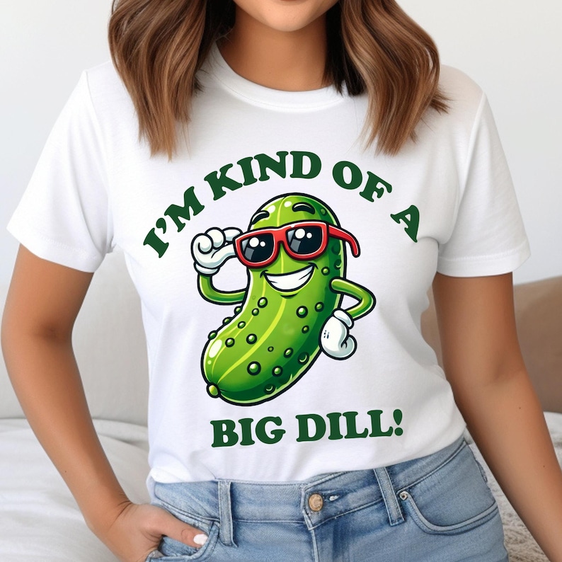 Może przedstawiać: Biała koszulka z zielonym kresk&oacute;wkowym og&oacute;rkiem w okularach przeciwsłonecznych i tekstem "I'm kind of a big dill!"
