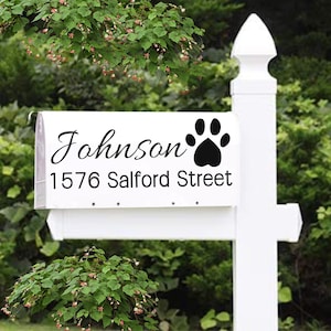 May include: White mailbox with the name "Johnson", a black paw print, and the address "1576 Salford Street" in black lettering. The mailbox is mounted on a white post, surrounded by green foliage.