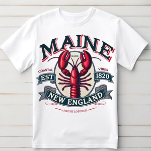 May include: White t-shirt with a graphic design featuring a lobster and the text "Maine Coastal Est 1820 Vibes New England Fresh Lobster".