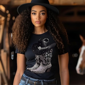 May include: Black t-shirt with a rhinestone cowboy hat and boots design. The design features a black cowboy hat with a silver band and a pair of black cowboy boots with rhinestones.