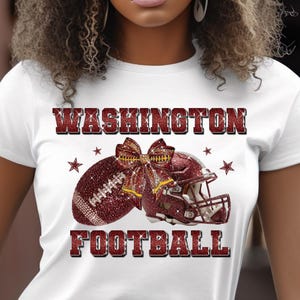 May include: White t-shirt with a Washington Football design. The design features a football, helmet, and text in a sparkling burgundy color. The word "WASHINGTON" is at the top, and "FOOTBALL" is at the bottom.