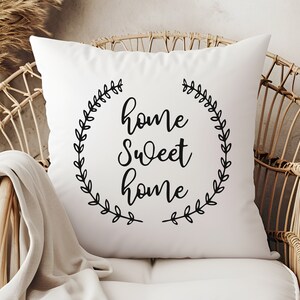 May include: White throw pillow with black text that reads "home sweet home" surrounded by a wreath of leaves.