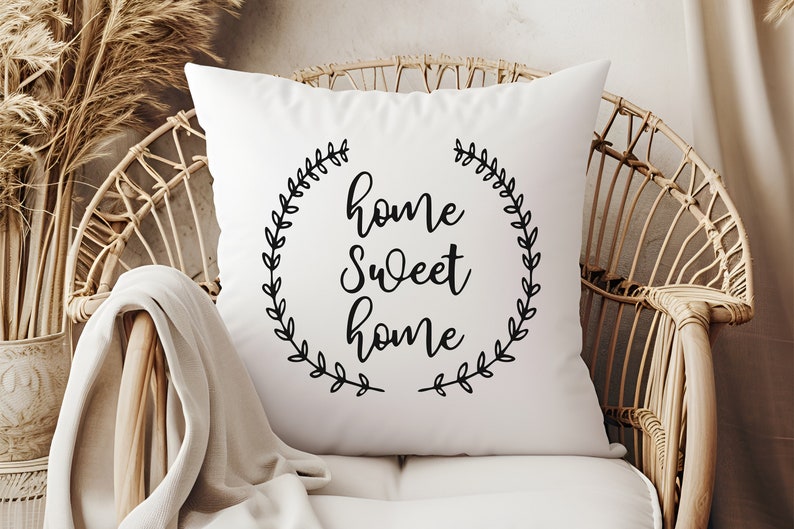 May include: White throw pillow with black text that reads "home sweet home" surrounded by a wreath of leaves.