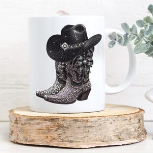 May include: White ceramic mug with a black cowboy hat and boots design. The boots and hat are covered in rhinestones.
