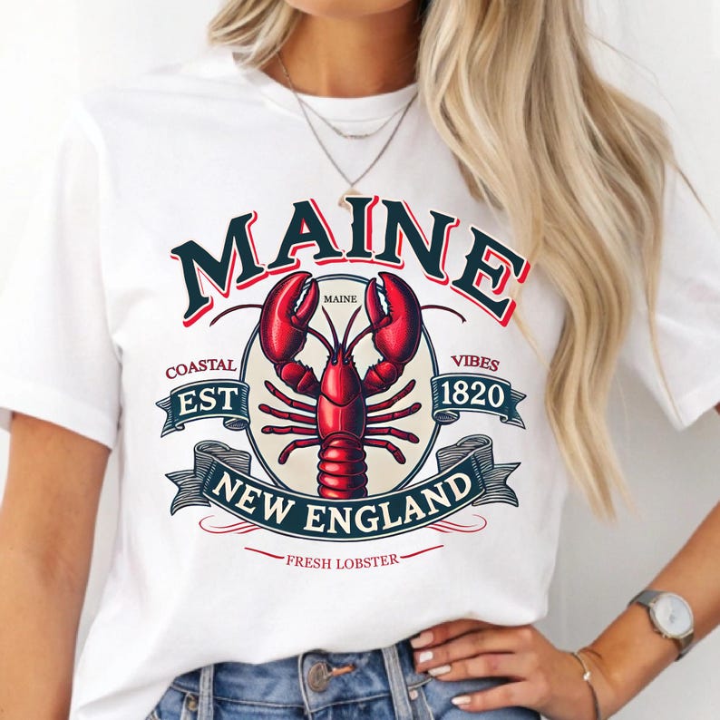 May include: White t-shirt with a vintage-style graphic design featuring a red lobster, the text "Maine", and the words "Coastal Est 1820 Vibes New England Fresh Lobster".