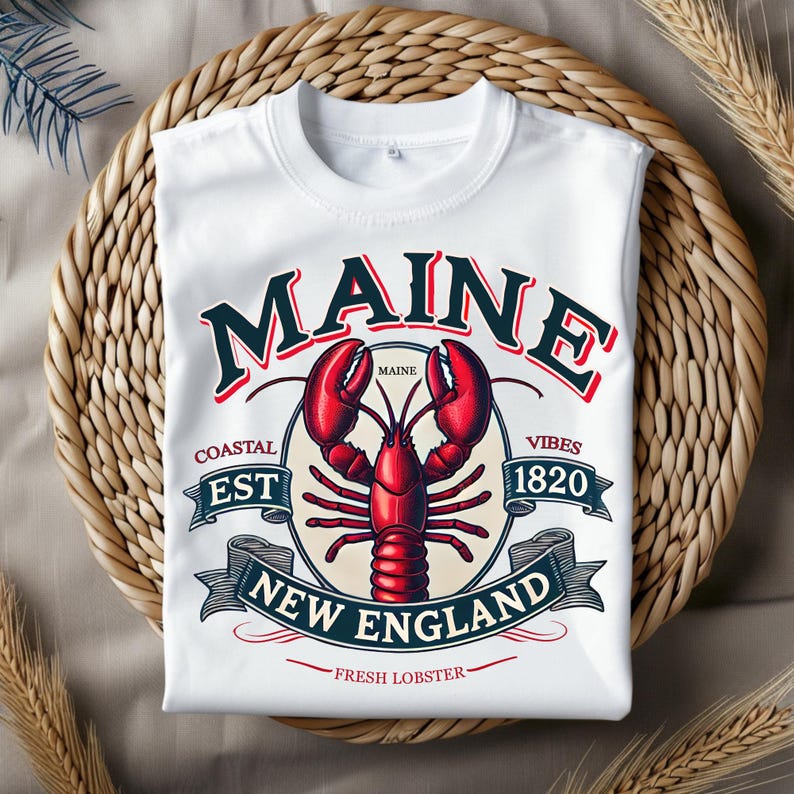 May include: White t-shirt with a vintage-style graphic design featuring a red lobster, the text "Maine", and the words "Coastal Est 1820 Vibes New England Fresh Lobster".