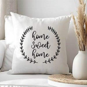 May include: White throw pillow with black text that reads "home sweet home" surrounded by a wreath of leaves.