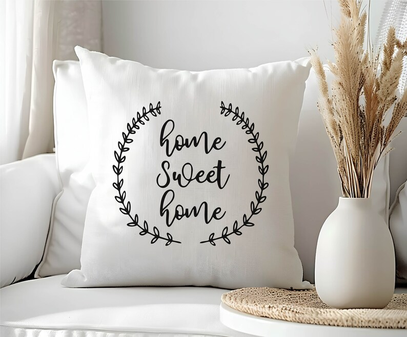 May include: White throw pillow with black text that reads "home sweet home" surrounded by a wreath of leaves.