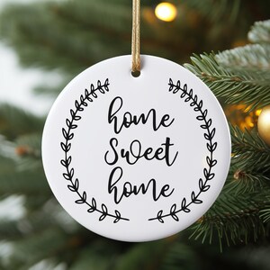 May include: White round ceramic ornament with a black wreath design and the text "home sweet home" in a cursive font.