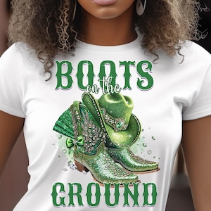 Op de afbeelding: Wit T-shirt met groene glitterlaarzen en een groene glittercowboyhoed. De tekst "Boots on the Ground" is op het shirt gedrukt.