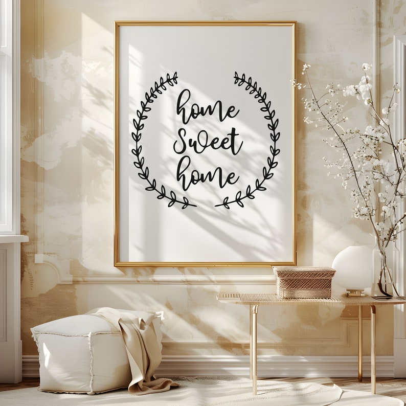 May include: A framed print with a white background and black text that reads "home sweet home" surrounded by a wreath of leaves. The print is hanging on a beige wall.