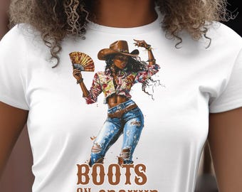 Puede incluir: Camiseta blanca con un gráfico de una mujer con sombrero de vaquero y vaqueros rotos, sosteniendo un abanico. La imagen tiene el texto "BOOTS ON THE GROUND" en letras marrones.