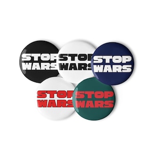 May include: A collection of five round buttons with the words "STOP WARS" in bold, white and red text. The buttons are in various colors: black, white, navy blue, and dark green.