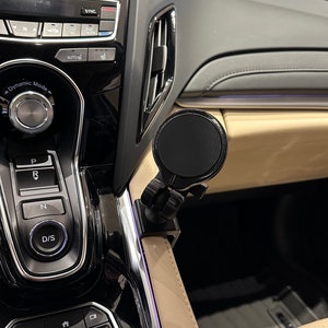 May include: A black car phone mount with a circular base and a swivel arm. The mount is attached to the dashboard of a car.
