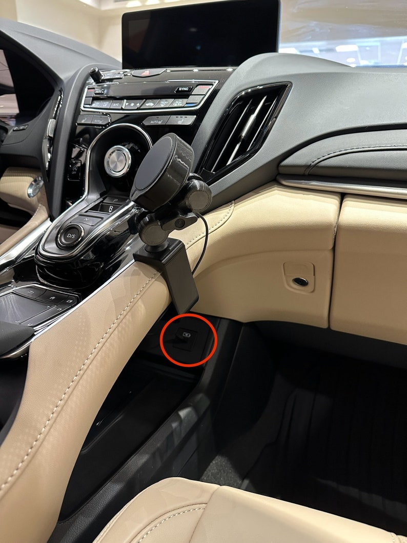 Puede incluir: Primer plano del interior de un coche negro con un soporte para tel&eacute;fono montado en el salpicadero. Un bot&oacute;n negro con un s&iacute;mbolo es visible en la consola central.