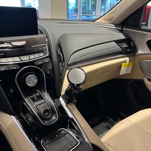 Puede incluir: Un interior de coche negro con un salpicadero negro y plateado y un asiento de cuero beige. El salpicadero tiene una pantalla t&aacute;ctil, una palanca de cambios y un panel de control con botones. El asiento est&aacute; hecho de cuero suave y flexible y tiene un patr&oacute;n de puntadas en forma de diamante.