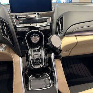 Puede incluir: Un interior de coche negro con una palanca de cambios negra y plateada, un panel de control negro y plateado y una pantalla negra y plateada. La pantalla est&aacute; en blanco. El coche tiene un interior de cuero beige.