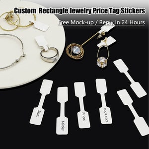 May include: White rectangular price tag stickers with a hole at the top for hanging. The stickers are blank and have the words "Size", "Price", "Logo", and "Your Text" printed on them. The stickers are shown on a black surface with jewelry.