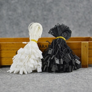 May include: Two bundles of string with plastic tags. One bundle is white string with white tags, the other is black string with black tags.