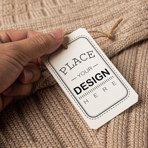 May include: A white tag with black text that says "PLACE YOUR DESIGN HERE" on a brown knitted fabric.