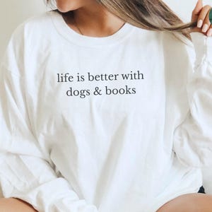 May include: A large white long-sleeve tee with the text "life is better with dogs & books" in black. The shirt has long sleeves and a crew neck. The words "LARGE WHITE LONG SLEEVE TEE" are printed at the bottom.