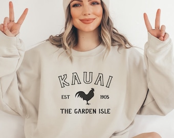 Könnte beinhalten: Ein hellbeiger Pullover mit einem schwarzen Grafikdruck eines Hahns und dem Text "KAUAI EST 1905 THE GARDEN ISLE"
