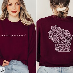 May include: A maroon sweatshirt with the word "Wisconsin" in white script on the front and a white outline of the state of Wisconsin filled with a floral pattern on the back.