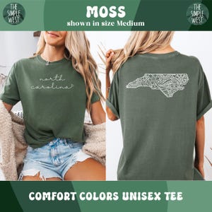 Pu&ograve; includere: T-shirt unisex Comfort Colors color muschio. La parte anteriore presenta la scritta "north carolina" in corsivo. Il retro mostra un contorno bianco dettagliato della Carolina del Nord. Il logo The Simple West &egrave; negli angoli superiori.