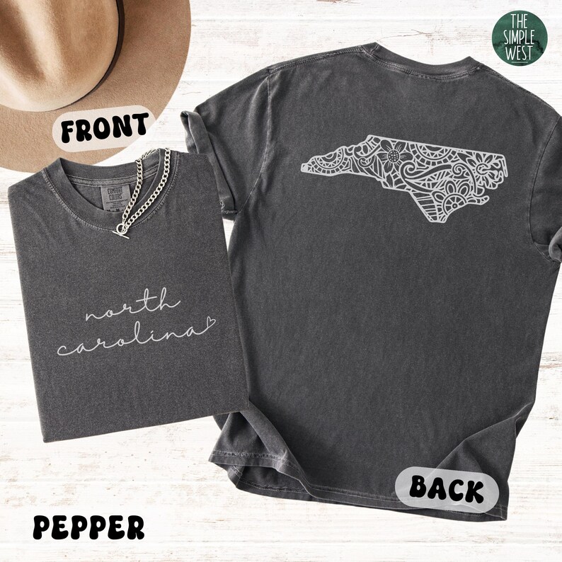 Pu&ograve; includere: T-shirt color pepe con la scritta "north carolina" sul davanti e un contorno bianco dettagliato della Carolina del Nord sul retro. Le magliette sono esposte con una collana a catena d'argento.