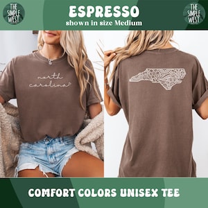 Pu&ograve; includere: T-shirt unisex Comfort Colors color Espresso. La parte anteriore presenta la scritta "north carolina" in corsivo. Il retro mostra un contorno bianco dettagliato della Carolina del Nord. La maglietta &egrave; mostrata in taglia Medium.