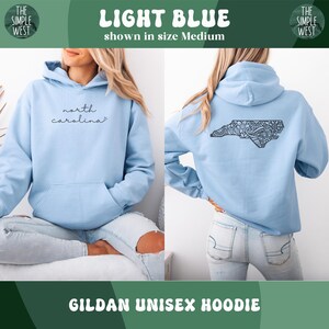 May include: Light blue Gildan unisex hoodie. The front features the text "north carolina" in a cursive font. The back displays a detailed black design of the North Carolina state outline. The hoodie is shown in size Medium.