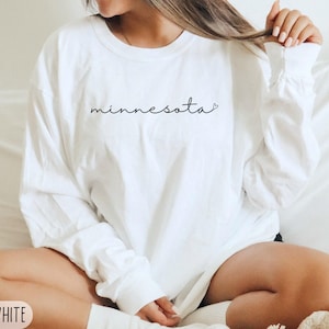 May include: White long-sleeve sweatshirt with the word "minnesota" in a cursive font. The sweatshirt is a large size and is white. The Simple West logo is in the top right corner.