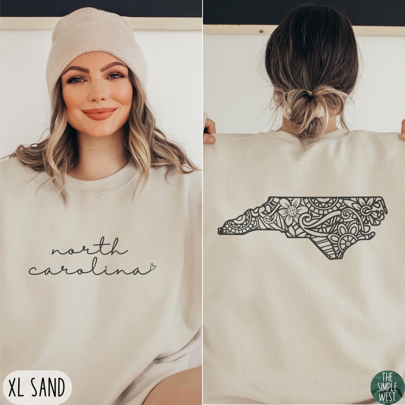 May include: A beige sweatshirt with the text "north carolina" on the front and a black and white mandala design of the state of North Carolina on the back. The sweatshirt is available in size XL and the colour sand.