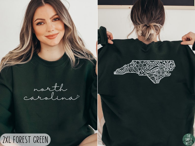 May include: Forest green sweatshirt with a white outline of the state of North Carolina featuring a floral design. The front of the sweatshirt has the text "north carolina" in white cursive writing with a heart.