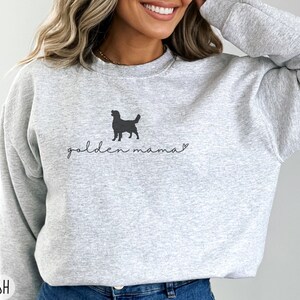 May include: Gray sweatshirt with a black silhouette of a golden retriever and the text "golden mama" in black.