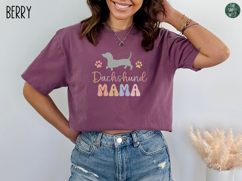 Puede incluir: Una camiseta corta de color malva con un gr&aacute;fico de un dachshund y el texto "Dachshund Mama" en letras de colores.
