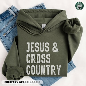 May include: An olive green hoodie with the text "JESUS & CROSS COUNTRY" in white. The hoodie is folded on top of a pair of blue jeans. The words "MILITARY GREEN HOODIE" are at the bottom of the image.
